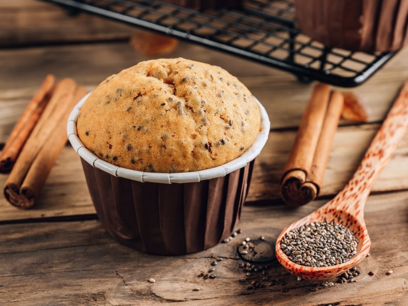 Ein Zimtmuffin. Daneben liegen ein Löffel Chiasamen und einige Zimtstangen.