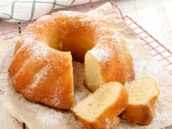 ein angeschnittener Apfelmuskuchen mit Zimt in Gugelhupfform, zwei Stücke liegen neben dem Kuchen. Nahaufnahme.