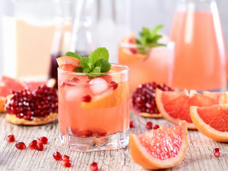 Mehere GlÃ¤ser und eine Karaffe Grapefruit-Granatapfel-Mocktail, daneben liegen die Zutaten.