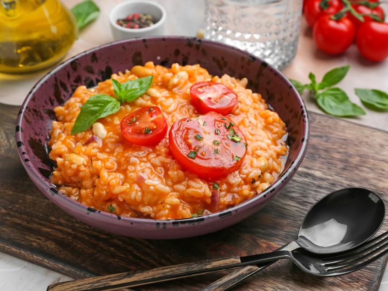 Italienischer Tomatenreis mit Bohnen in einer Schüssel, garniert mit Tomatenscheiben und Basilikum. Drumherum einige Zutaten.