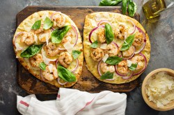 Zwei Stück Knoblauch-Naan mit Garnelen, garniert mit Basilikum und roter Zwiebel.