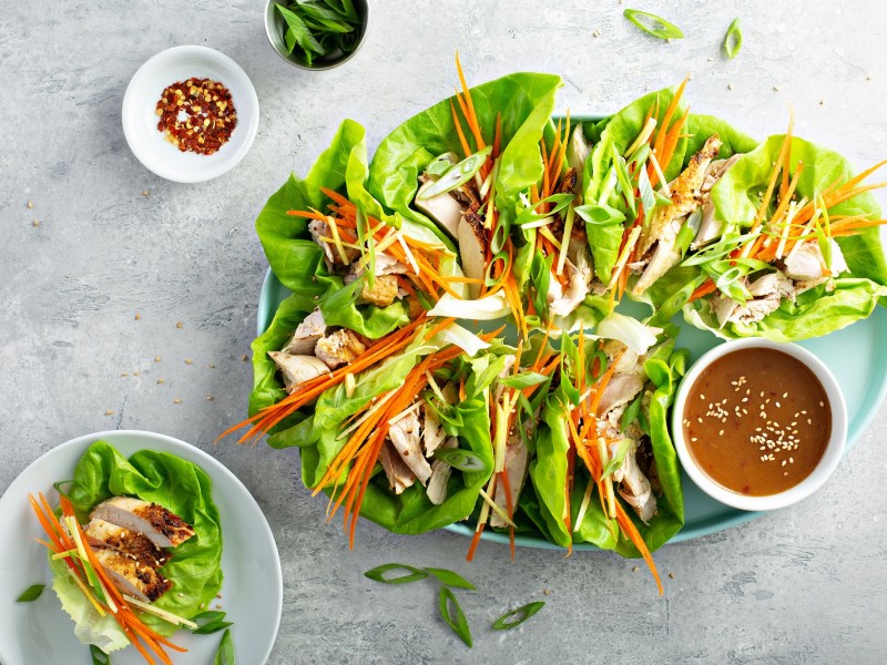 Ein großer Teller mit Salat-Wraps mit Huhn und einem Dip.