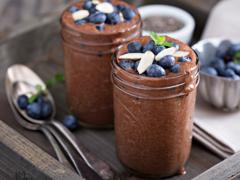 Zwei Gläser Schoko-Chia-Pudding, garniert mit Beeren und Mandeln.