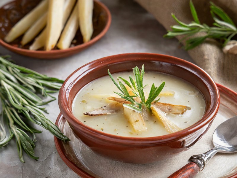 Schale mit Schwarzwurzel-Cremesuppe, Schwarzwurzeln und KrÃ¤uter daneben