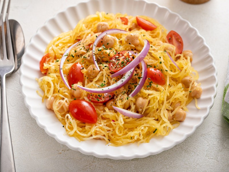 Ein Teller zubereiteter SpaghettikÃ¼rbis mit Tomaten und Kichererbsen.