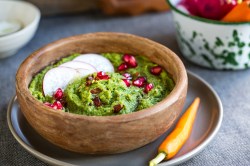 Eine Schüssel Spinat-Hummus, serviert mit Granatapfelkernen und Radieschenscheiben.