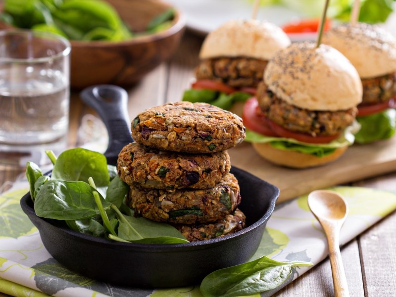 Vegane Bohnen-Burger in einer gusseisernen Pfanne. Dahinter weitere Burger.