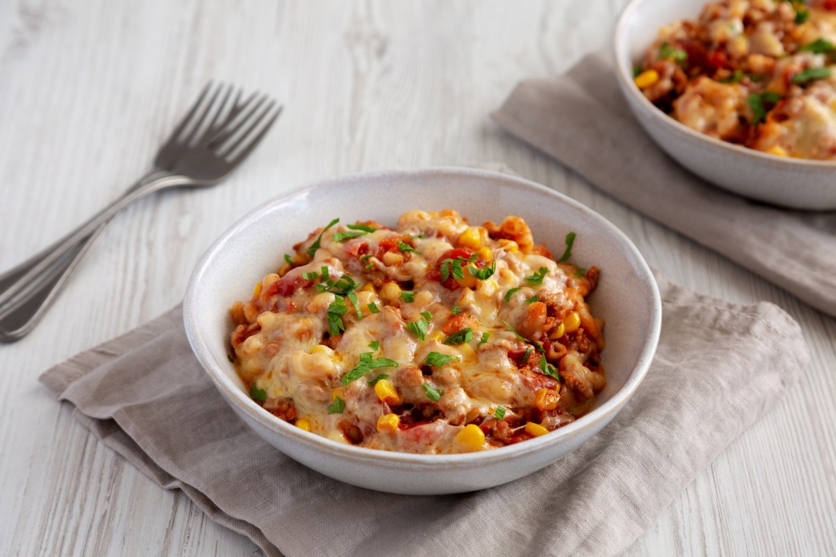 Ein weißer Teller voll mit veganer One Pot Taco Pasta, der auf einer grauen Stoffserviette steht. Schräg links daneben liegen zwei Gabeln. In der rechten oberen Bildecke kann mit verschwommen einen weiteren Teller mit veganer One Pot Taco Pasta erkennen.