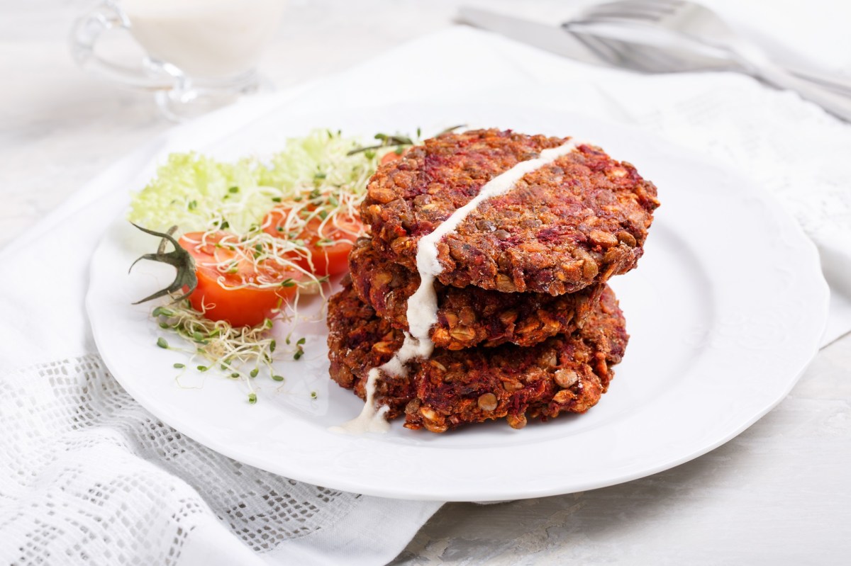 Vegane Rotkohlbratlinge mit Haferflocken liegen auf einem weißen Teller. Daneben liegt etwas Gartenkresse und eine halbierte Tomate.