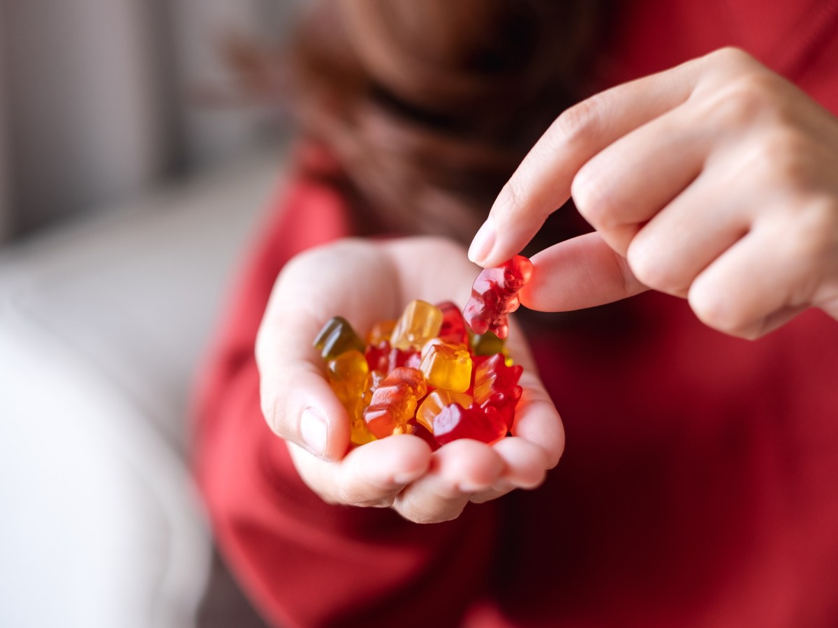 Vegane Süßigkeiten: eine Frau isst Gummibärchen aus ihrer Hand, man sieht nur ihre Hände und ihrem Oberkörper.