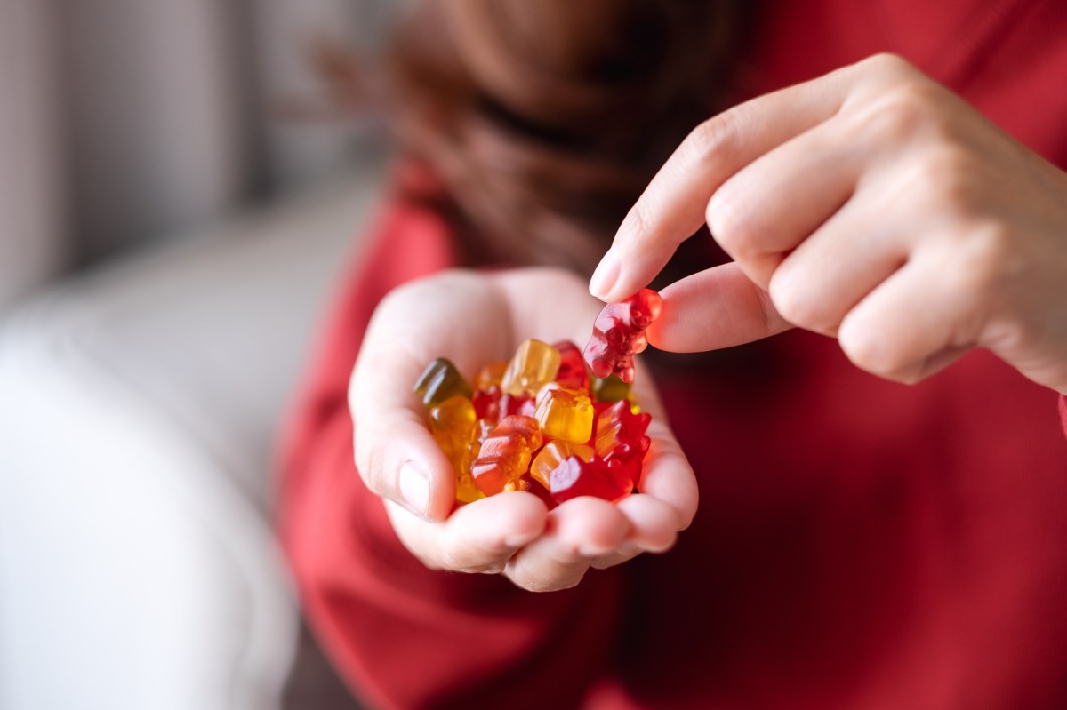 Vegane Süßigkeiten: eine Frau isst Gummibärchen aus ihrer Hand, man sieht nur ihre Hände und ihrem Oberkörper.