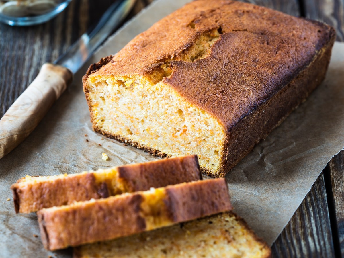 Veganer Chai-Kuchen liegt angeschnitten auf einem Stück Backpapier auf einem dunklen Holztisch.