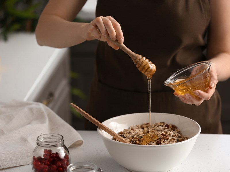 Eine Frau süßt ihr Müsli mit veganem Honig, man sieht nur ihre Hände und ihren Oberkörper.