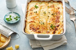 Veganes Kartoffelgratin in weißer Auflaufform, mit Kräutern bestreut, drumherum einige Zutaten.