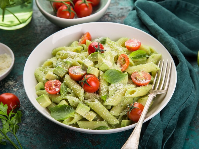 Avocado-Nudelsalat in einem tiefen Teller, serviert mit Parmesan und Tomaten.