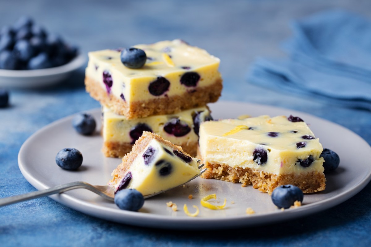 Mehrere Stücke zuckerfreier Zitronen-Heidelbeer-Kuchen auf einem Teller. Drum herum liegen Blaubeeren.
