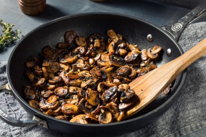 Champignons mit Kräuter-Chili-Soße in einer Pfanne mit einem Holzlöffel. Nahaufnahme.