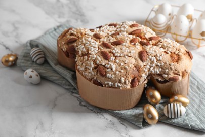 Colomba Pasquale: italienischer Osterkuchen in Taubenform in einer Papierhülle. Drum herum liegen dekorative Ostereier. Der Kuchen steht auf einem Leinentuch, das wiederum auf einer Marmorplatte drapiert ist.