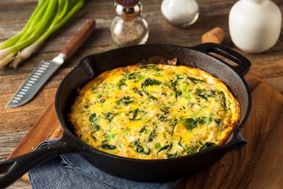 Feta-Spinat-Omelett in einer Pfanne, drumherum einige Zutaten und ein Messer.