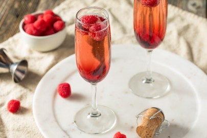 Zwei Gläser Kir Royal mit Himbeeren auf einem weißen Marmortablett.