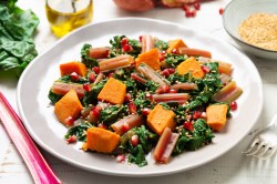 Ein Teller lauwarmer Süßkartoffel-Mangoldsalat mit Granatapfelkernen und Sesam, drumherum einige der Zutaten.