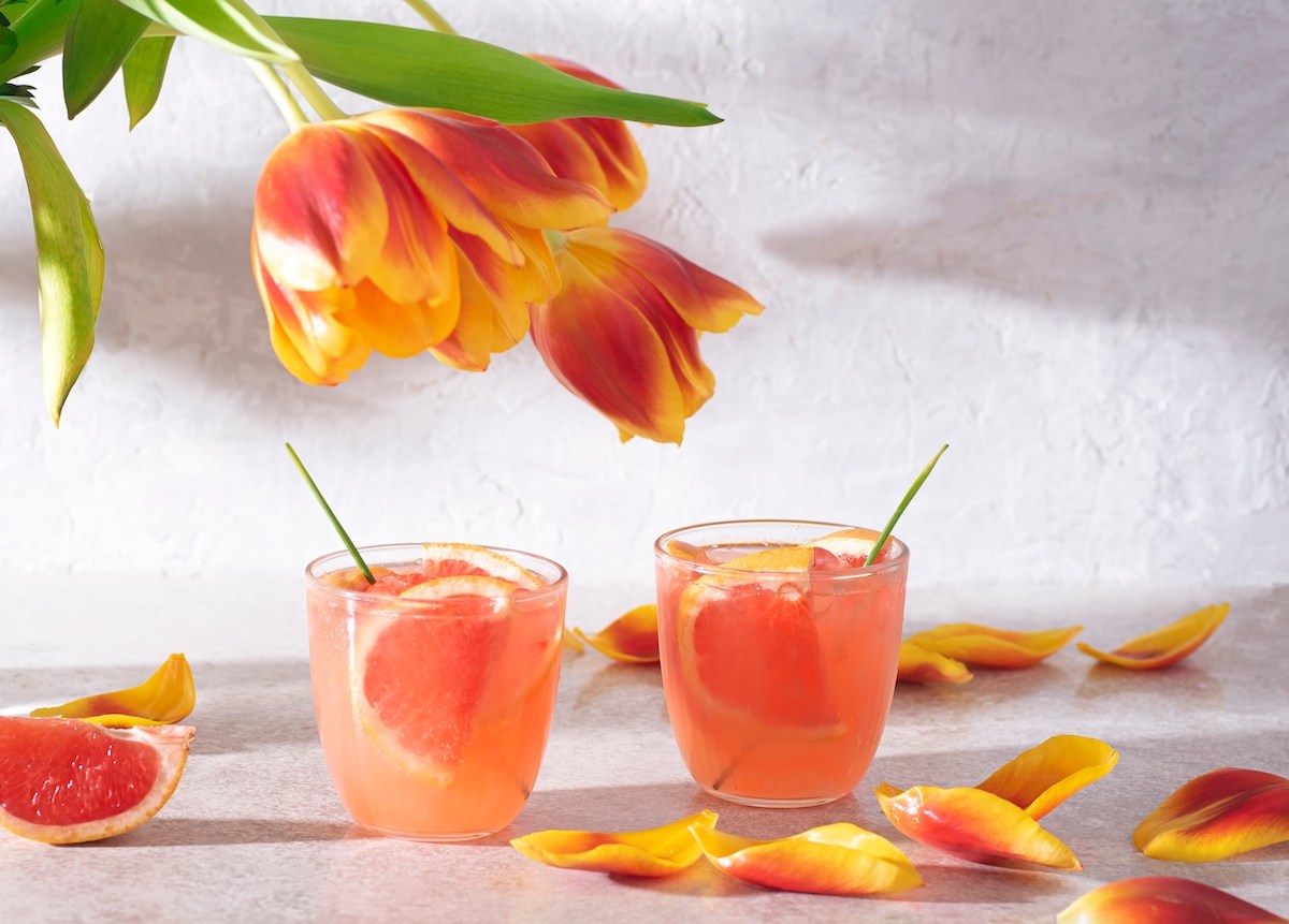 2 Gläser Martini Tonic garniert mit frischer Grapefruit, daneben ein paar Tulpen.