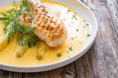 Ein Teller Spargel mit Miso-Hollandaise und einem Stück Hähnchenbrust. Nahaufnahme.